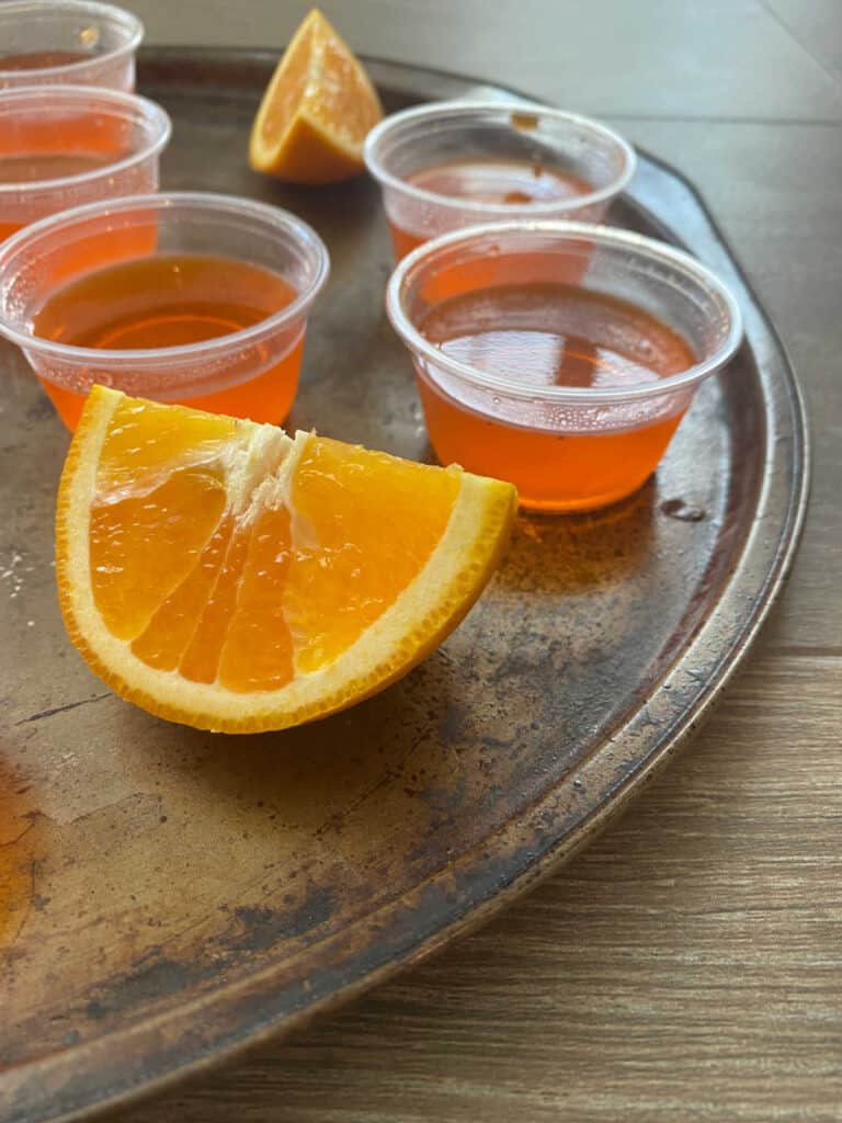 Close up of jello shots on a dark pan with an orange segment garnish.