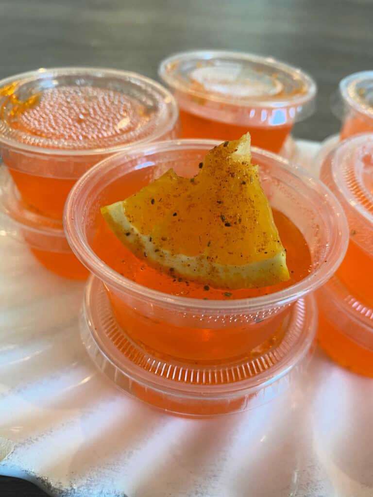 One jello shot in a stack is opened, topped with an orange segment, sprinkled with Old Bay.