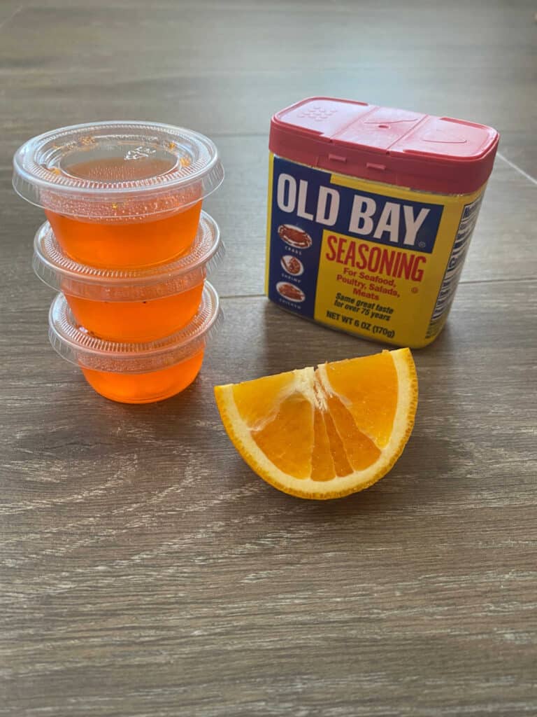 Stack of 3 jello shooters with a orange segment and can of Old Bay next to them.