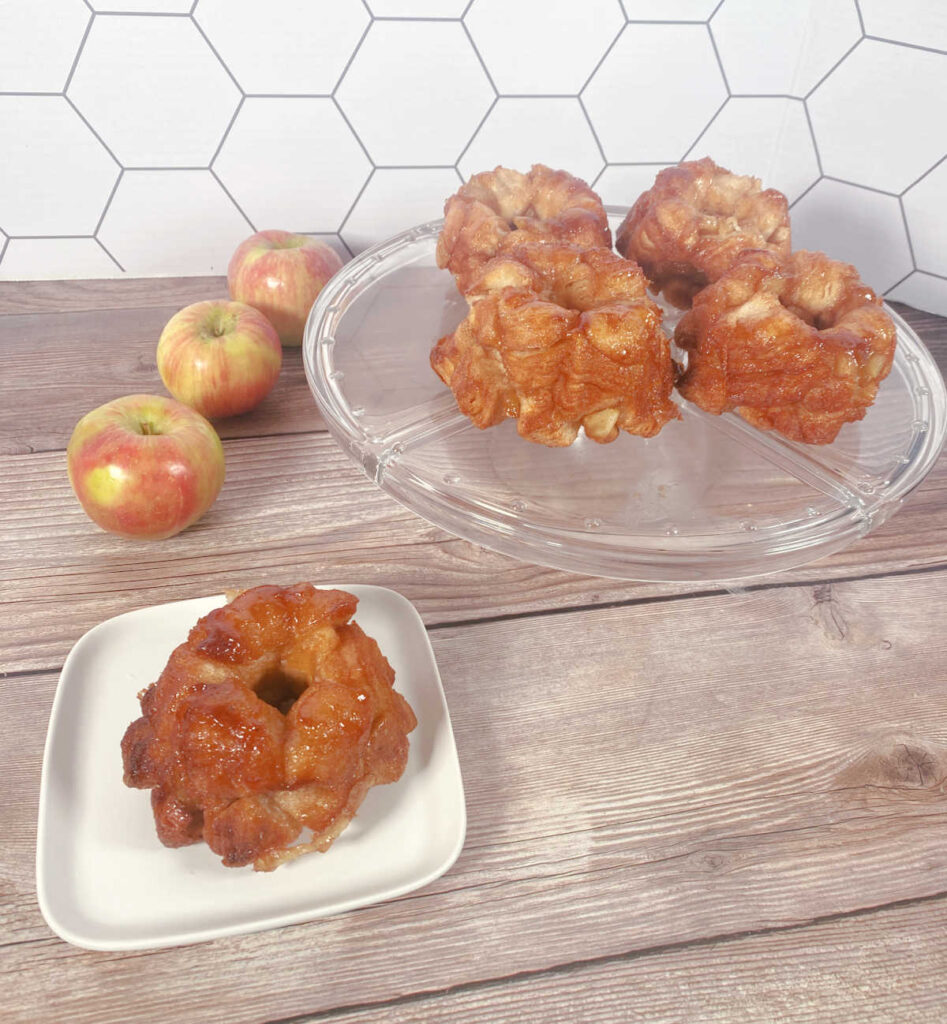 Over image of single monkeybread on a square white plate with other desserts on a glass cake tray. 