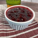 Cranberry sauce in a white ramekin with a bottle of bourbon behind it.