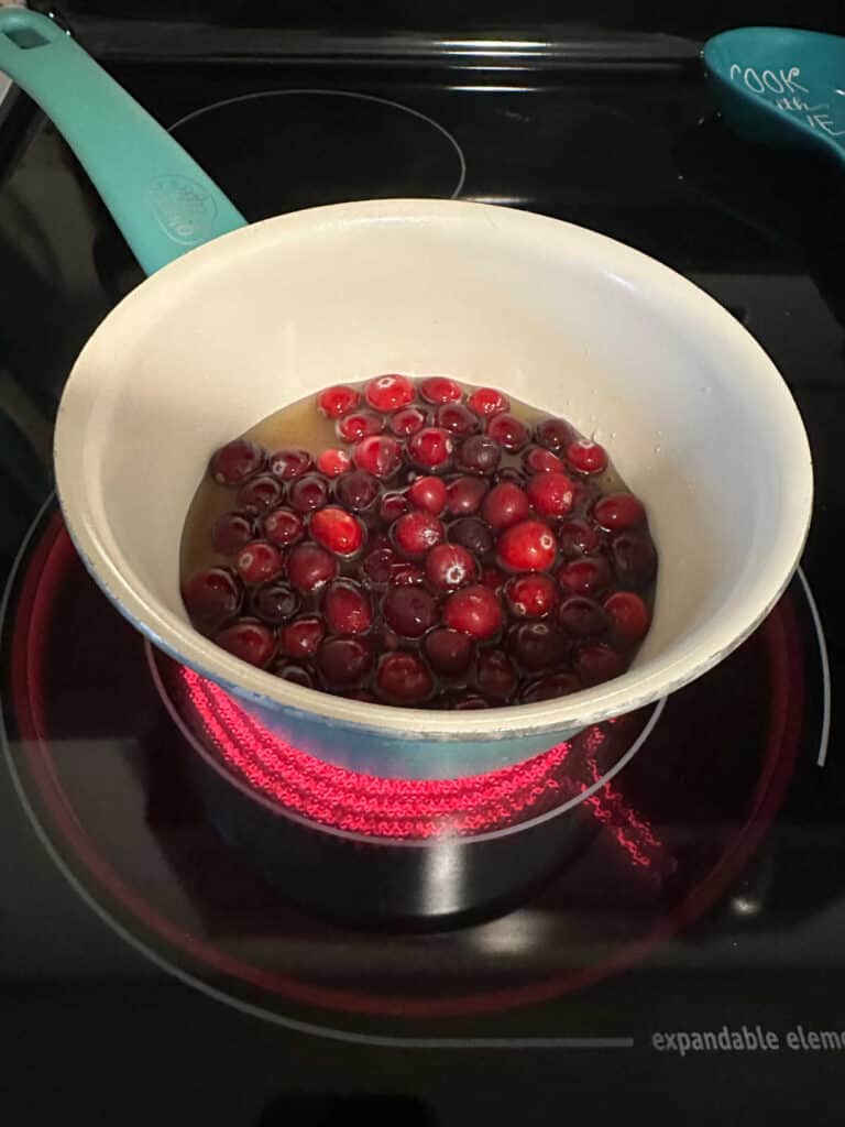 Process shot - cranberries in a blue pot on the stove. 