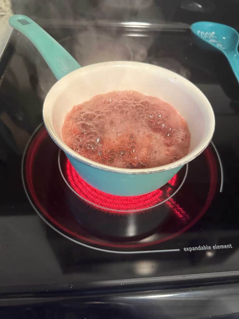 Process shot - simmering cranberries in a blue pot on the stove. 