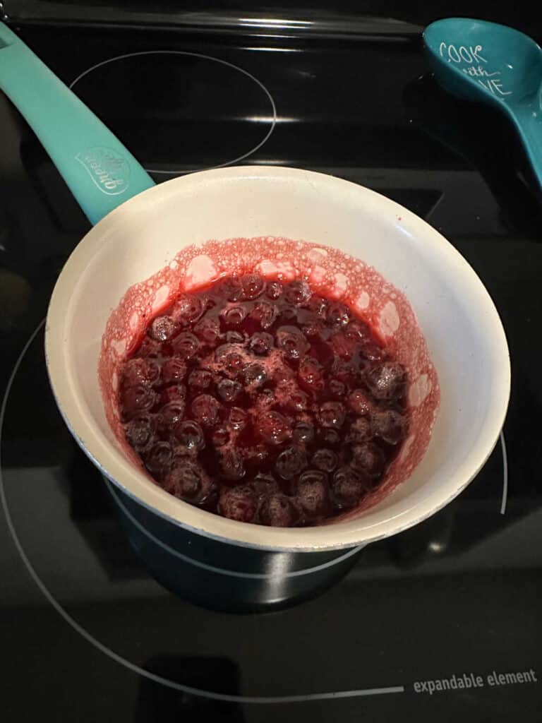 Process shot - thickening cranberry sauce sits on a pot on the stove.