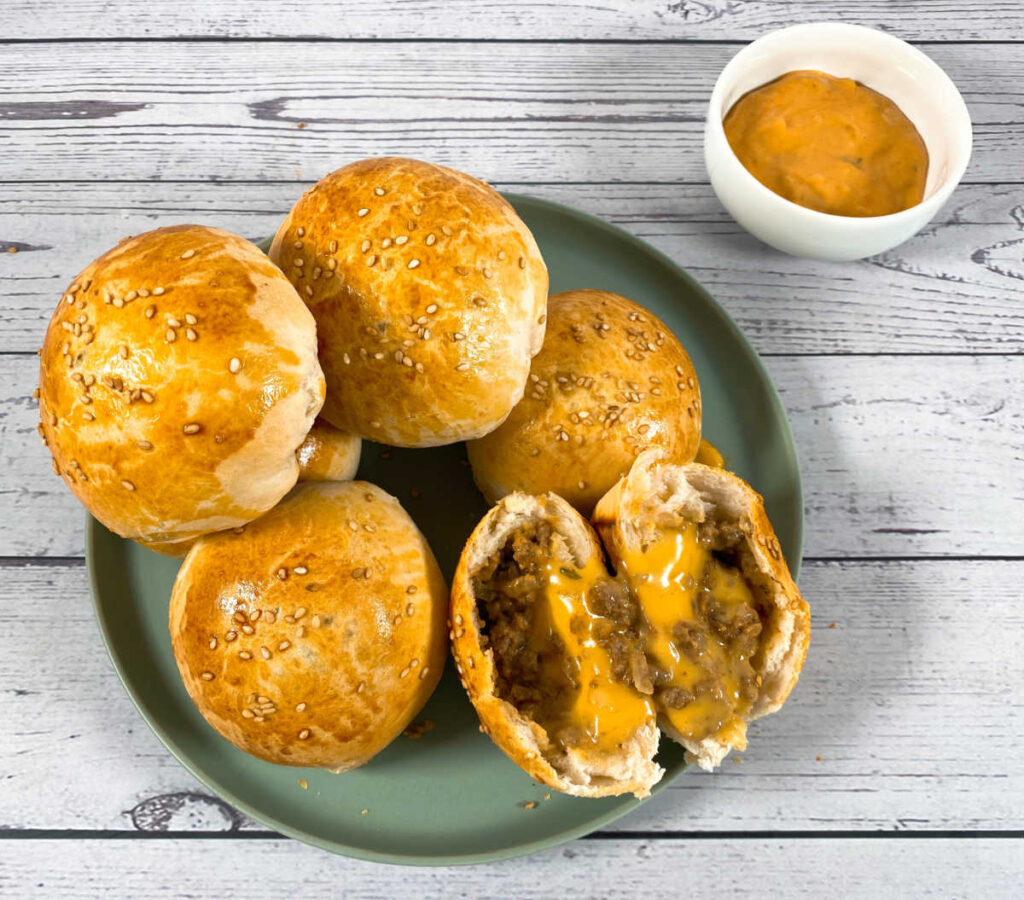 Plate of burger bombs, with one sliced open to show the melted cheese inside.