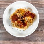 bowl of cheesy meatballs and sauce sits on a bed of pasta in a white round dish.