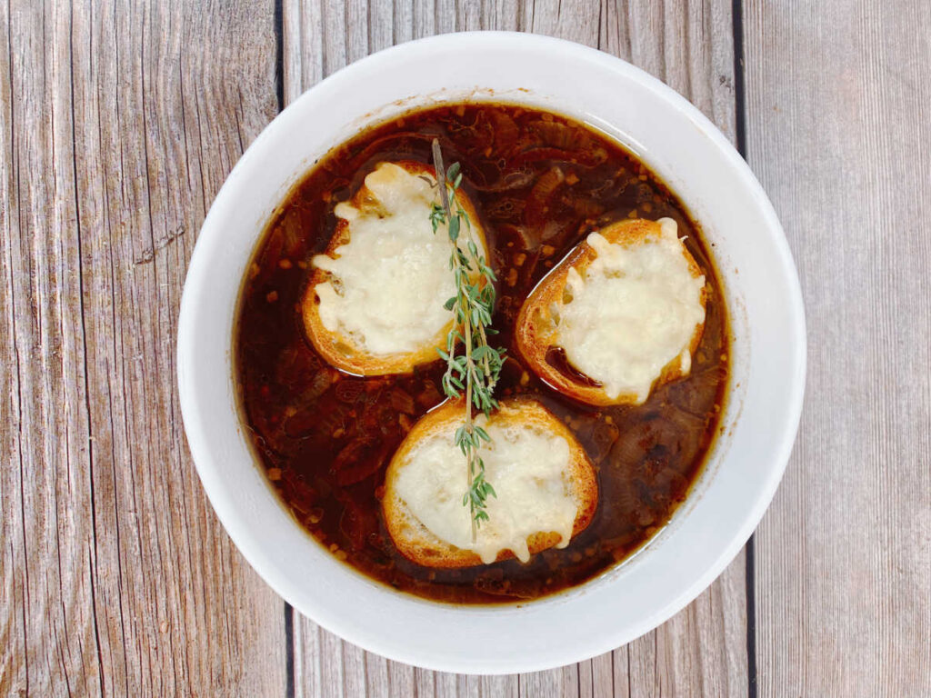 Overhead shot of bowl of soup with three pieces of cheesy toast and a fresh thyme garnish. 