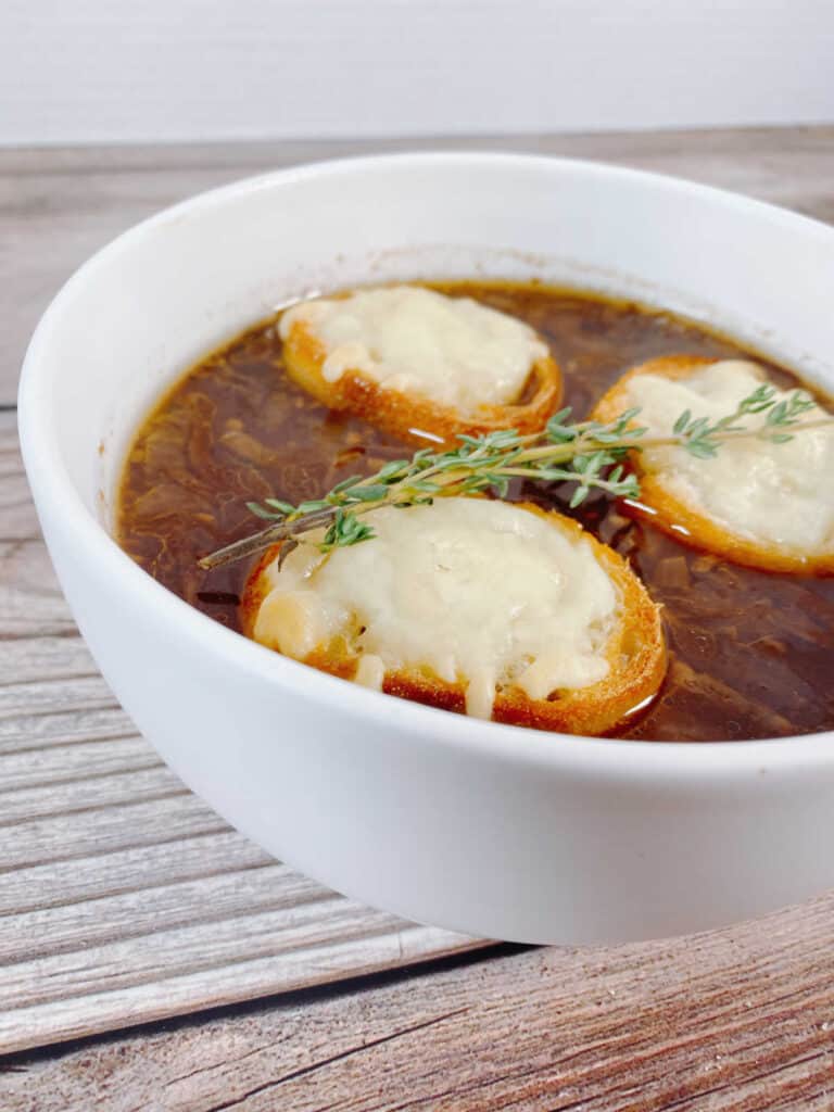 Angled image of soup in a white bowl, zoomed in on the cheesy toast floating on top. 