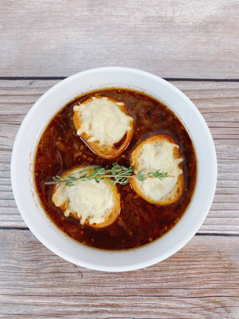 overhead image of soup in a white bowl with 3 pieces of chees toast and fresh thyme sprig.