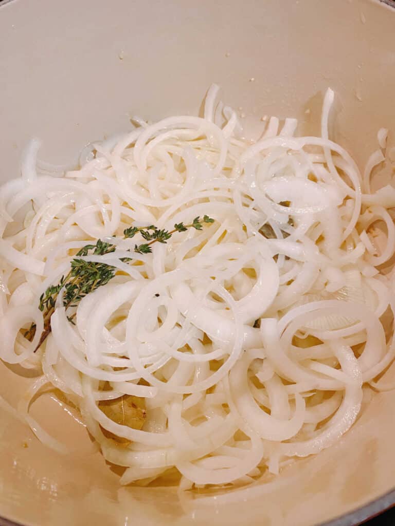 Process shot - sliced onions in pot with thyme, bay leaf and garlic. 