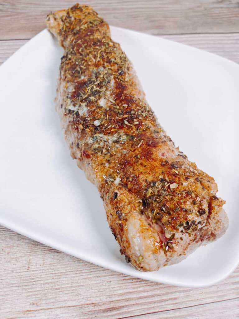 Process shot - tenderloin resting on a plate, waiting to be sliced and garnished. 