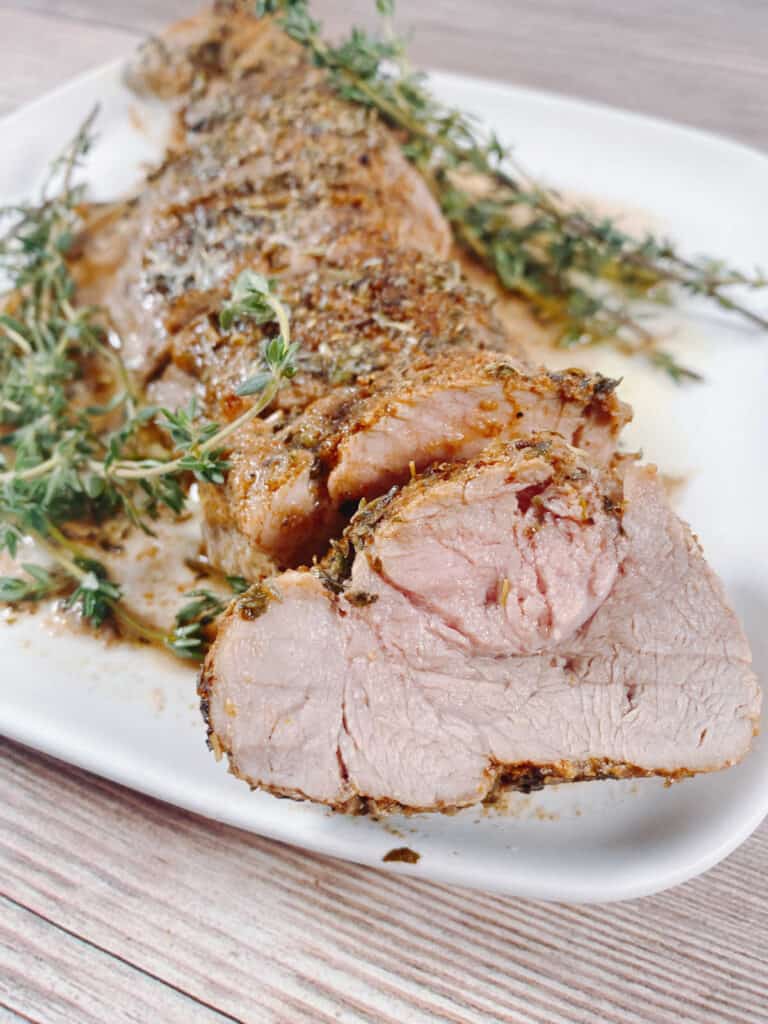 Slices of pork tenderloin topped with fresh herbs sit on a white plate.