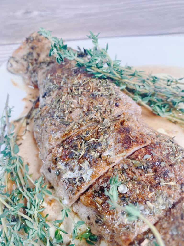 Close up of spices and herbs on the pork, fresh thyme sits off to the side. 