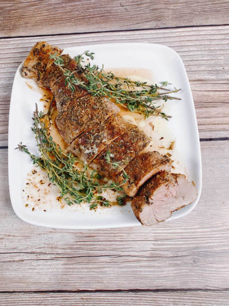 Sliced tenderloin, garnished with fresh herbsm on a white plate. 