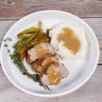 Slices of pork tenderloin with herb and potatoes on a round white plate.