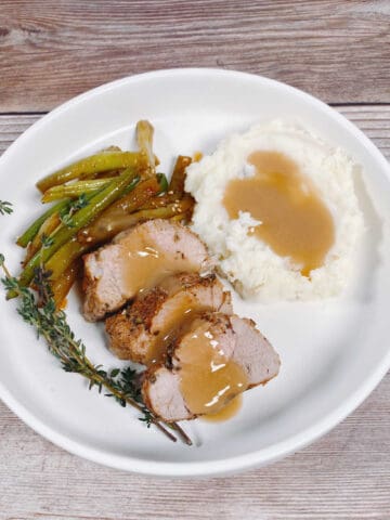 Slices of pork tenderloin with herb and potatoes on a round white plate.