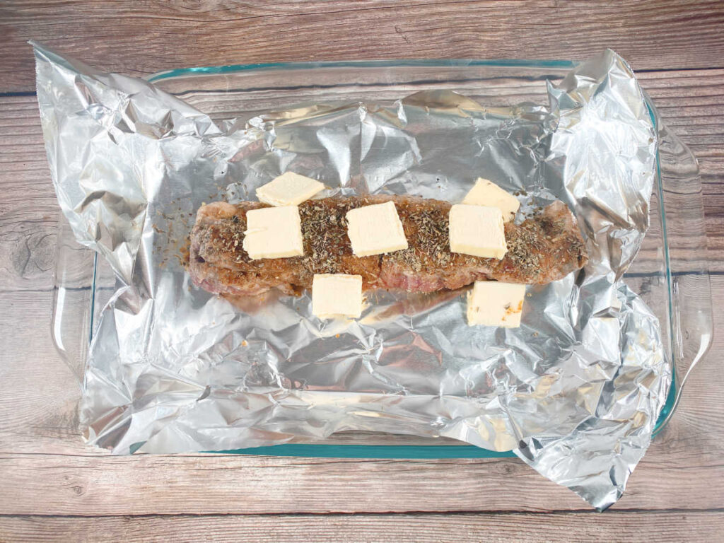 Pork in baking dish with dried herbs and butter, ready to finish in oven. 