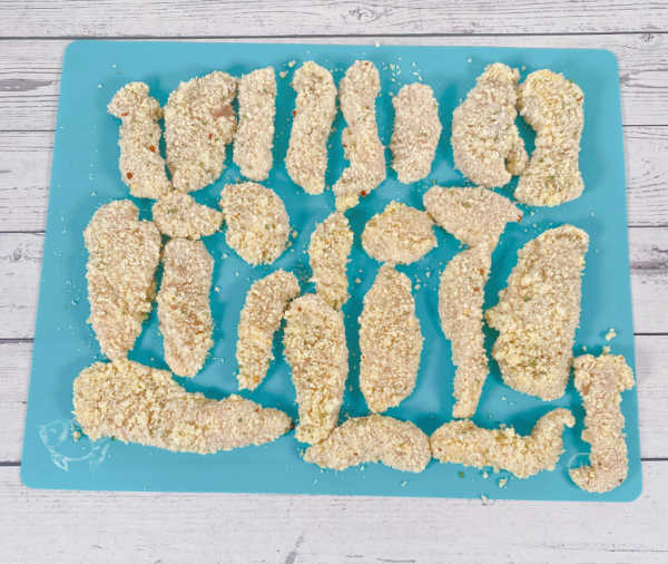 Process shot - dredged chicken tenders sitting on a blue cutting board. 