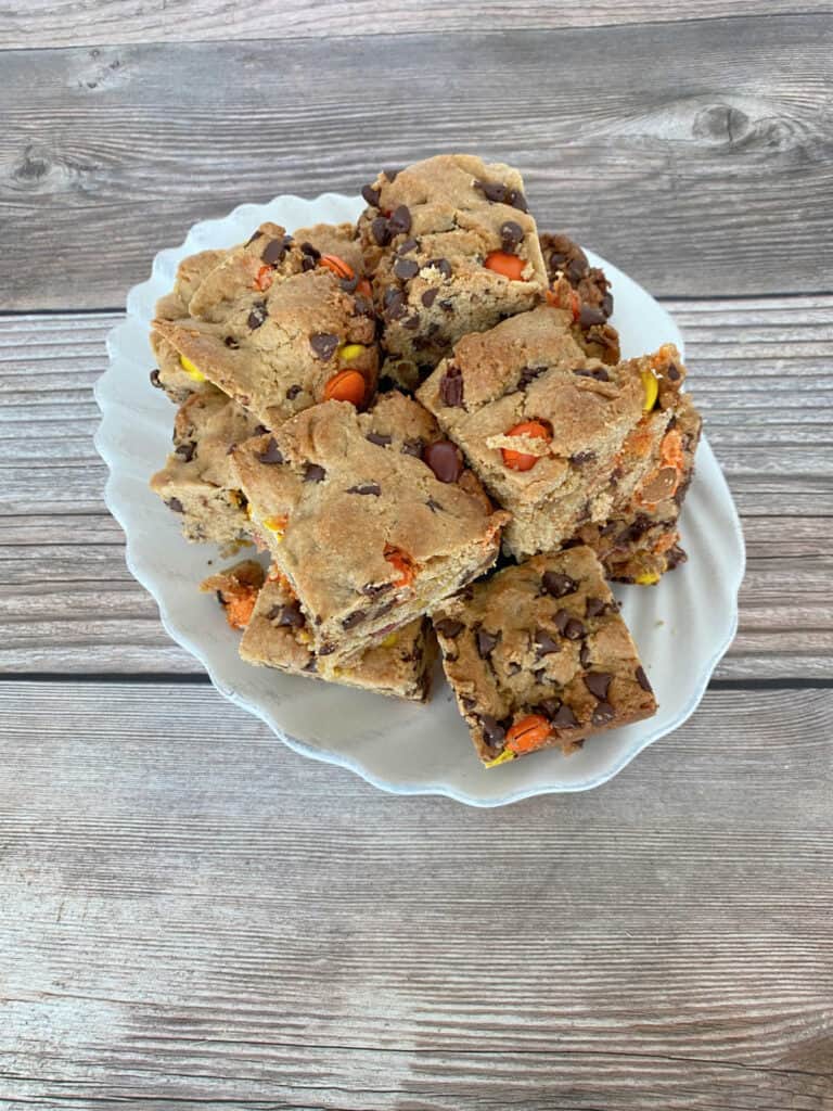 Stack of cookie bars sits on a white scalloped plate on a wooden background. 