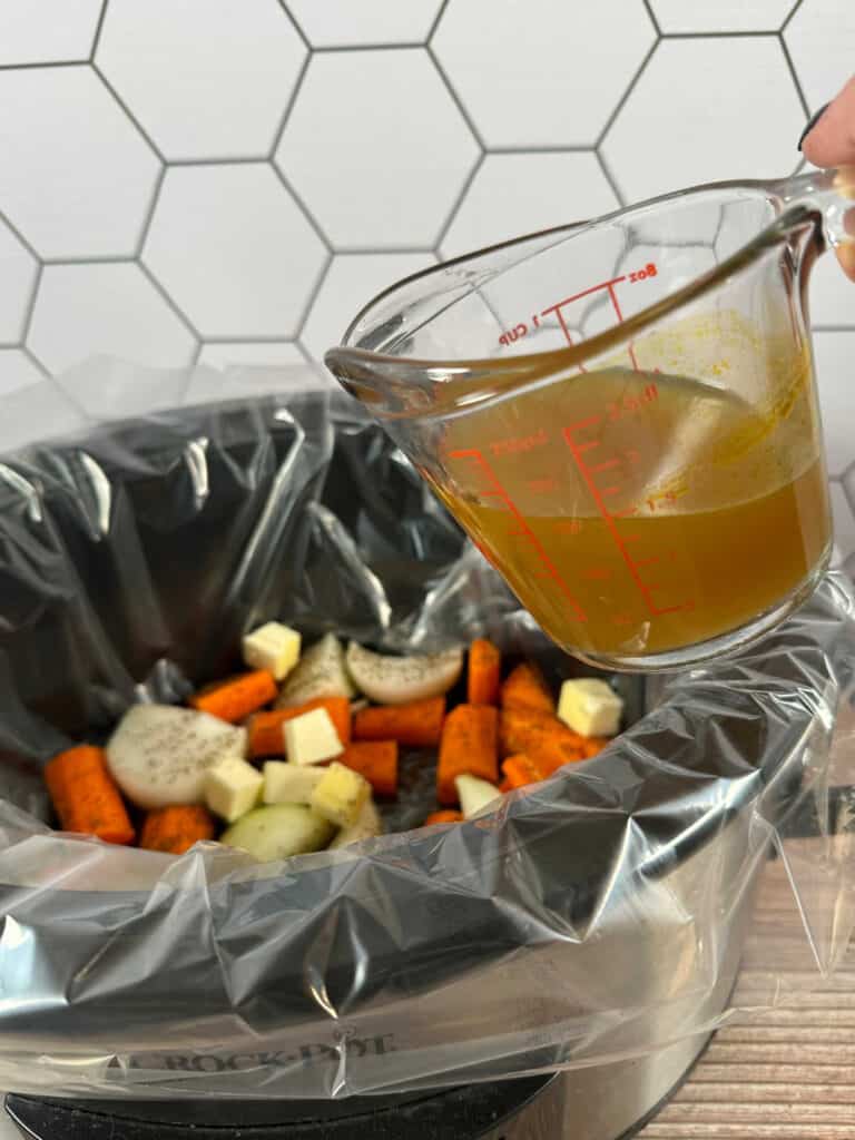 Process shot - chicken broth in glass measuring cup being poured into the slow cooker. 