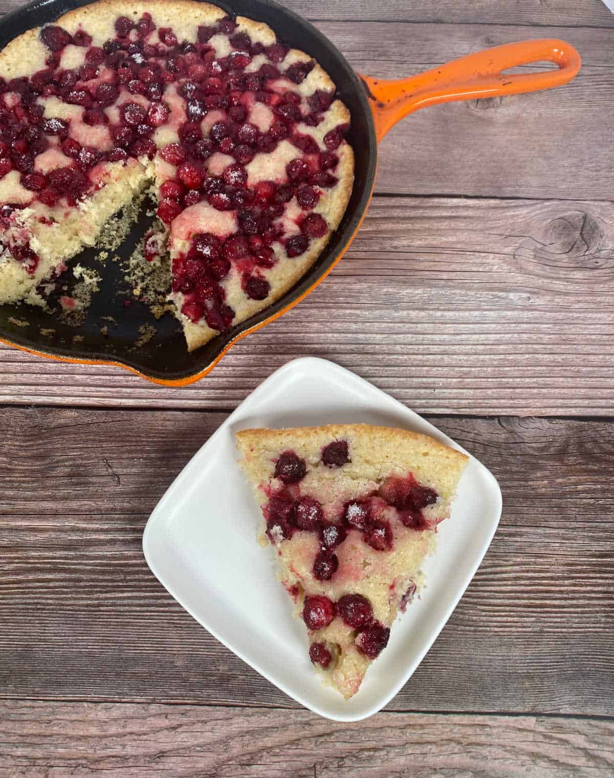 Slice of cobbler sits on a white plate with whole cobbler behind it. 