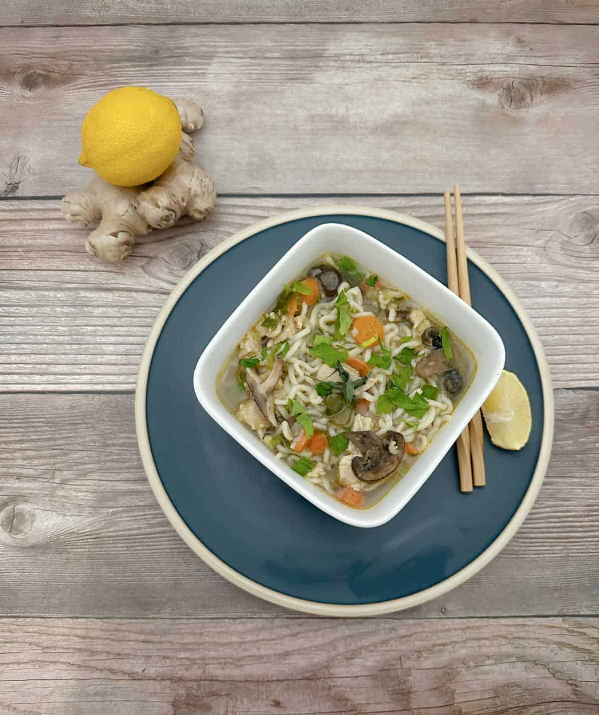 Overhead image of soup in a square white bowl. Fresh ginger and lemon sit off to the side. 