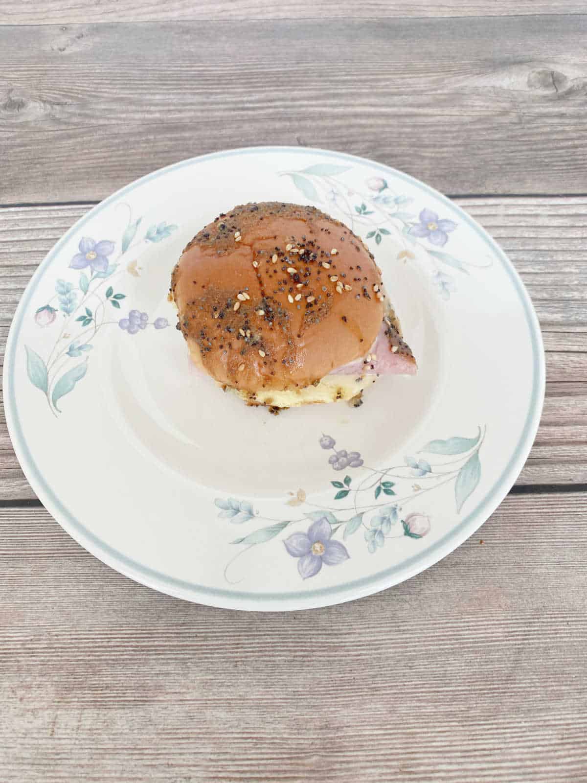 Slider sandwich sits on a white, floral printed round plate on a wooden background. 