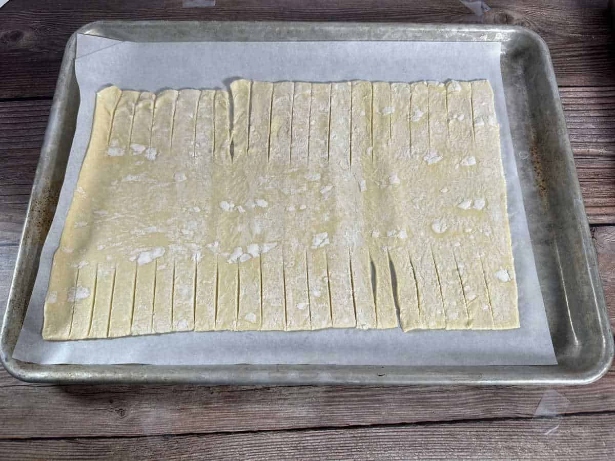 Pastry on parchment paper lined baking sheet with lines cut for braiding. 