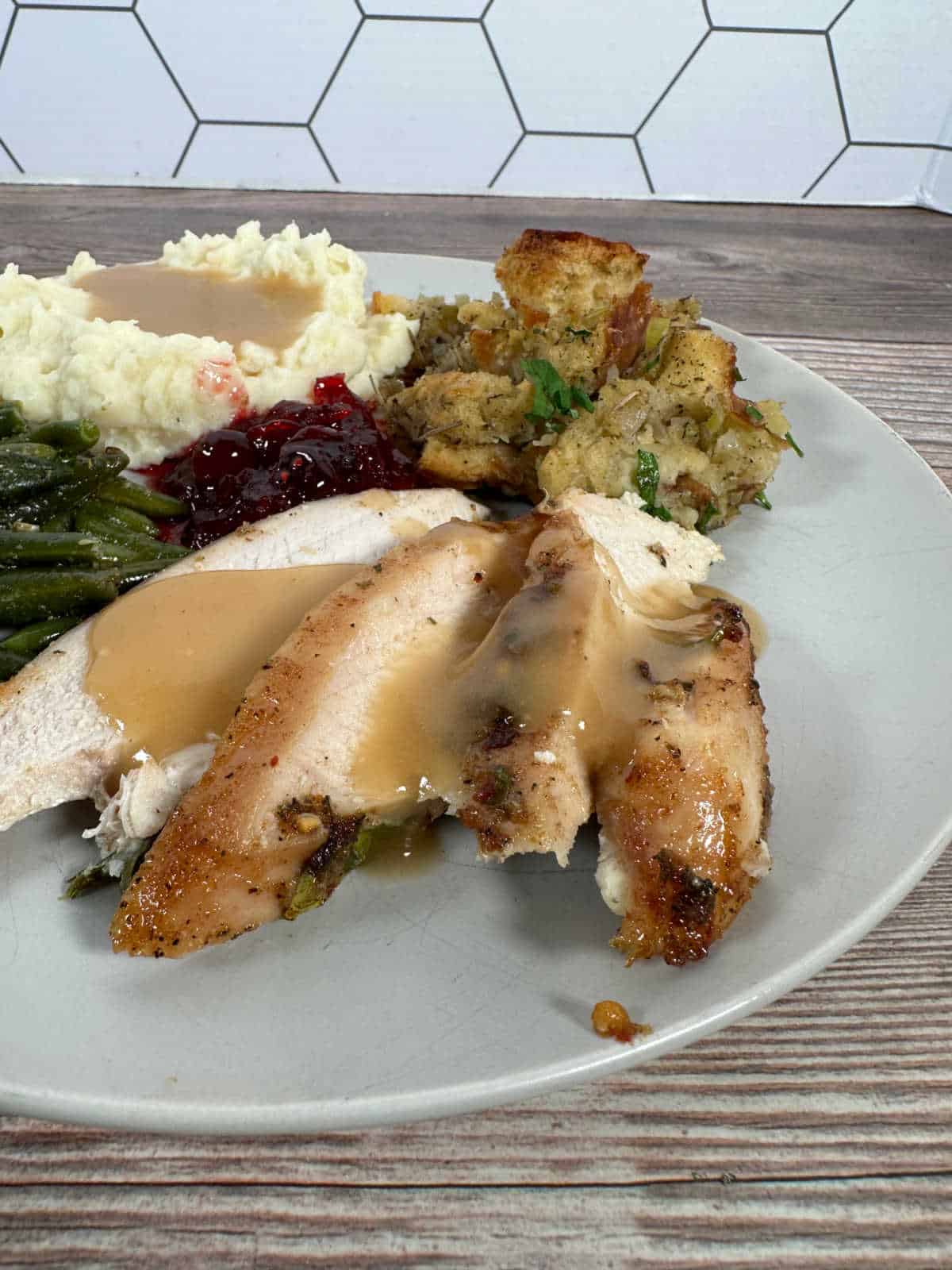 Slices of turkey, topped with gravy sit on a plate surrounded by traditional Thanksgiving side dishes.