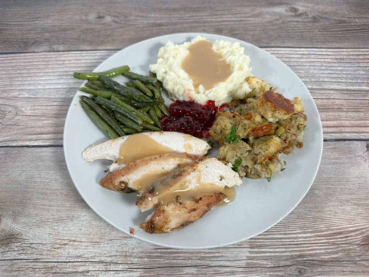 Sliced turkey breast with gravy sits on a light blue plate surrounded by traditional Thanksgiving side dishes.