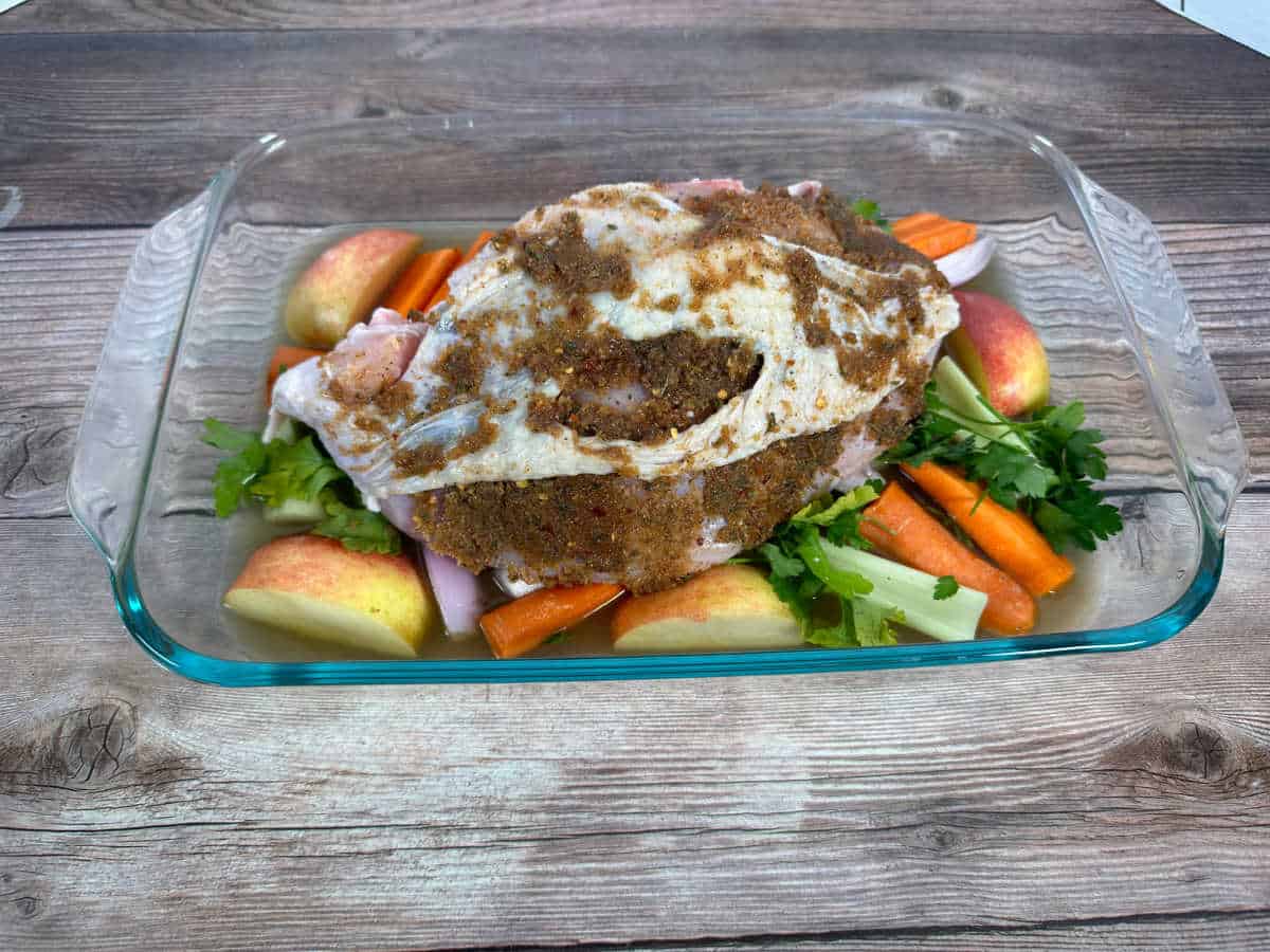 Turkey, coated with the rub, sits on top of the vegetables in the baking dish waiting to be cooked. 