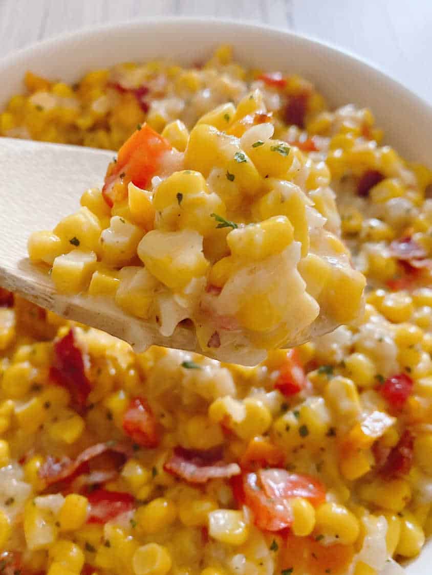 Close up image of a wooden spoon lifting the corn mixture out of a white round bowl. 