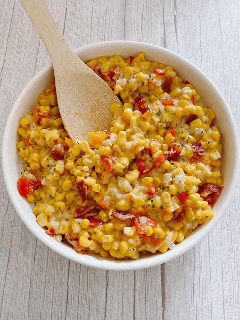 Wooden spoon lifts corn mixture out of a white round bowl. 