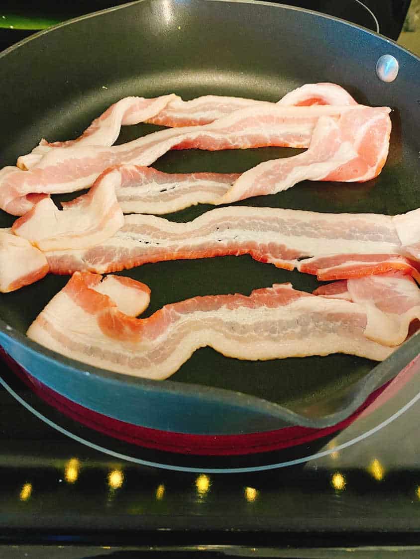 Process shot - slices of bacon in a large skillet. 