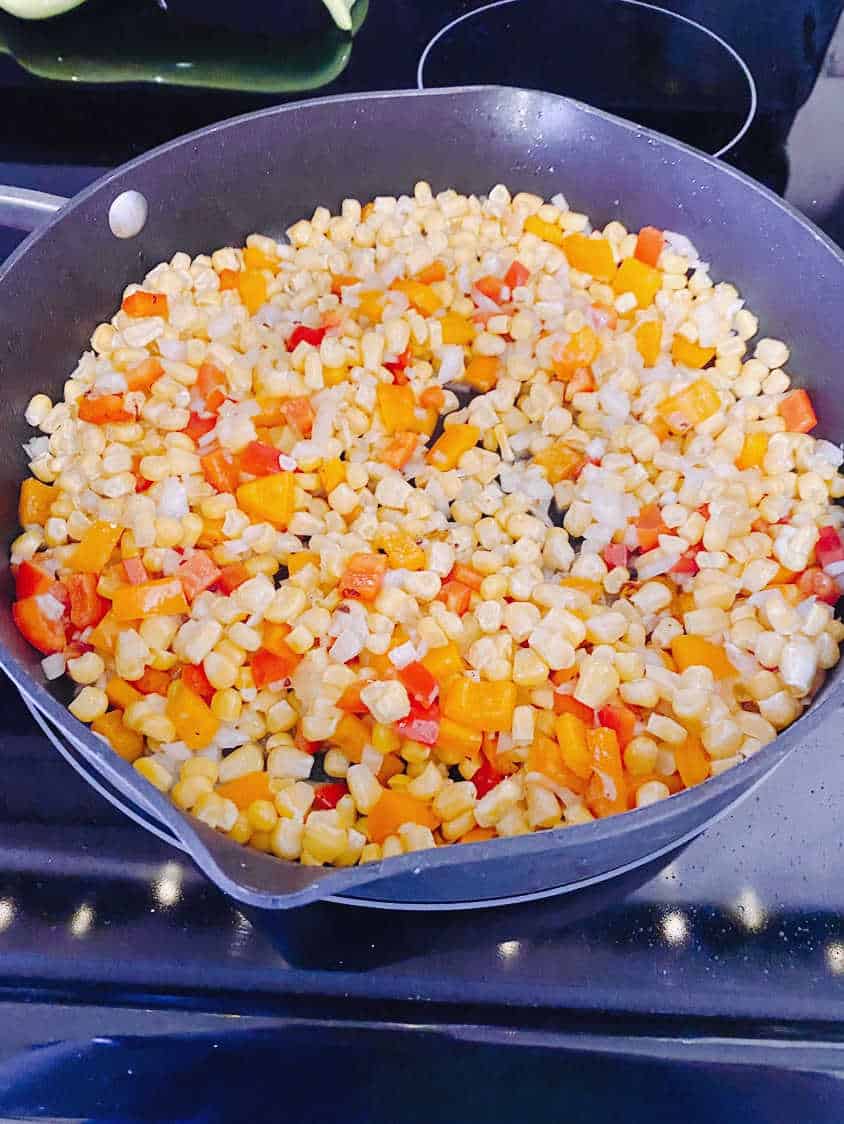 Process shot - corn, bell peppers and onions cooking in a skillet. 