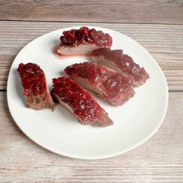 Slices of pork tenderloin topped with cranberry sauce sit on a round, white plate.