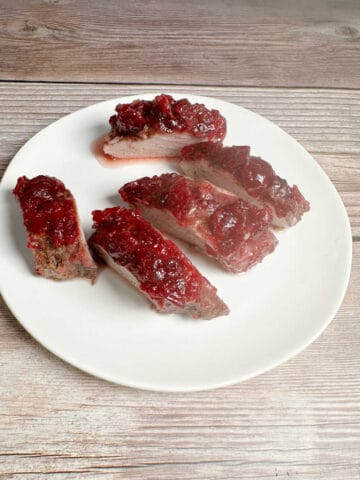 Slices of pork tenderloin topped with cranberry sauce sit on a round, white plate.