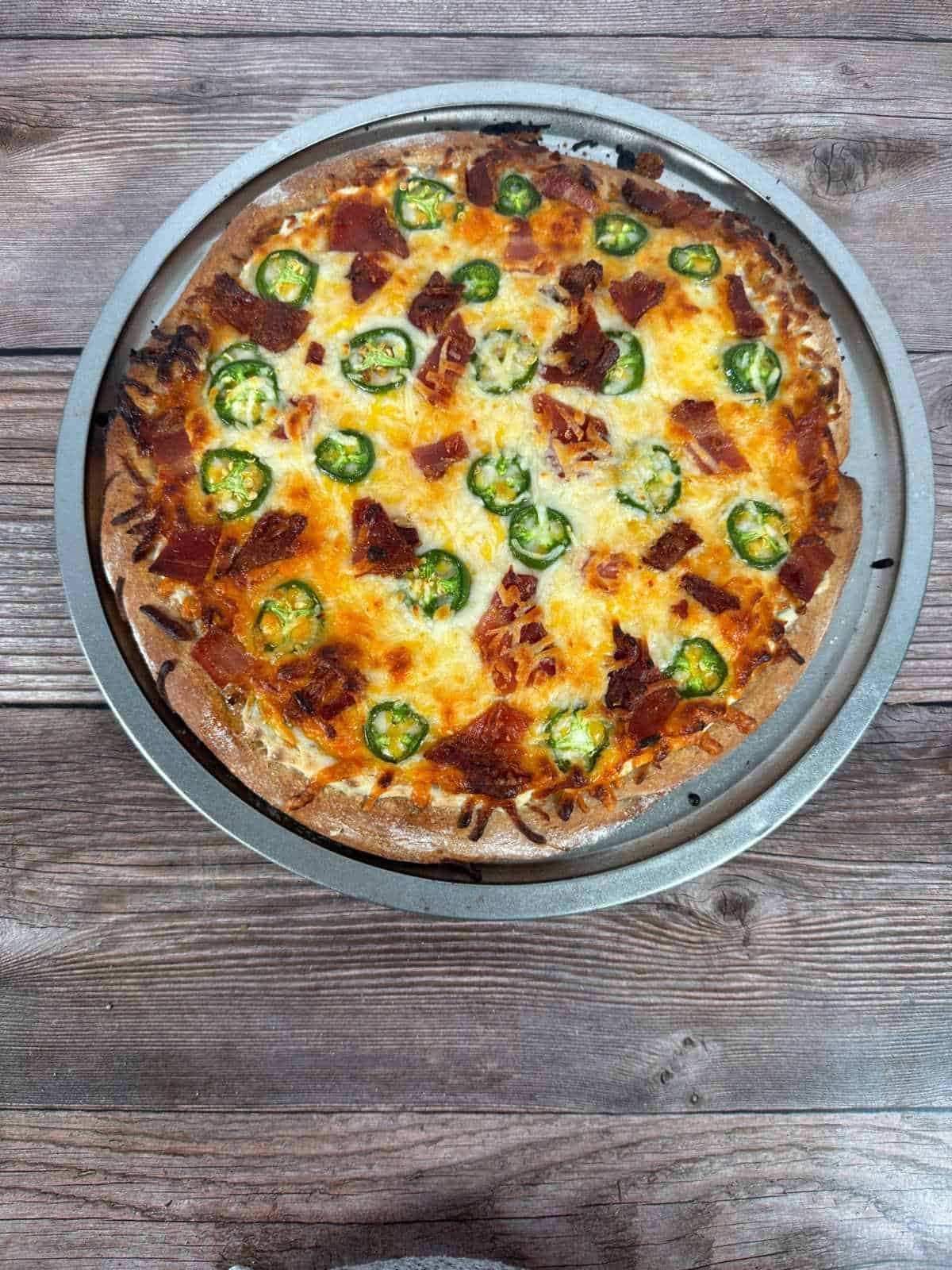 Overhead image of baked pizza on a wooden background before being sliced. 