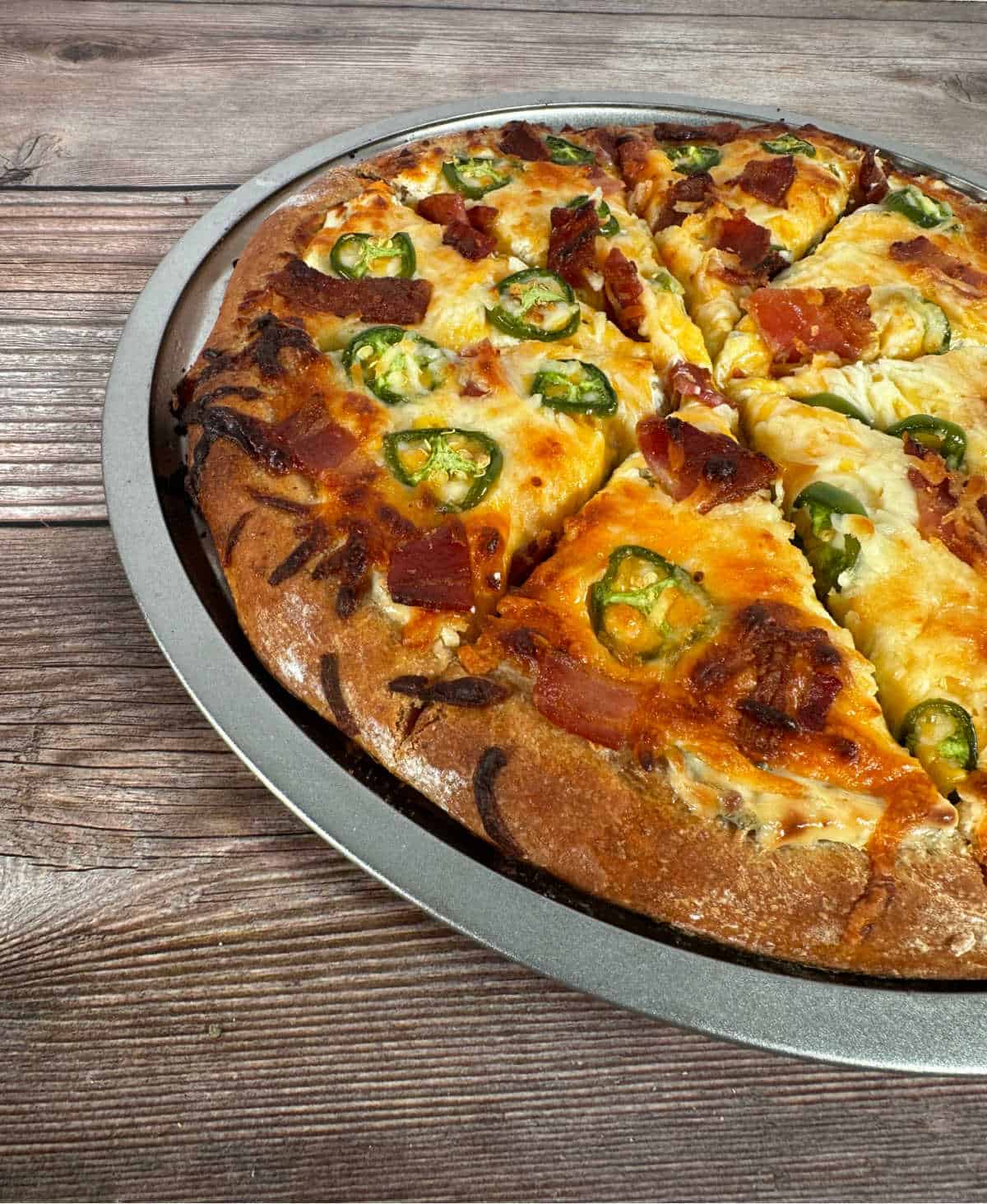 Side view of pizza showing the melted cheese and jalapenos and bacon nestled in. 