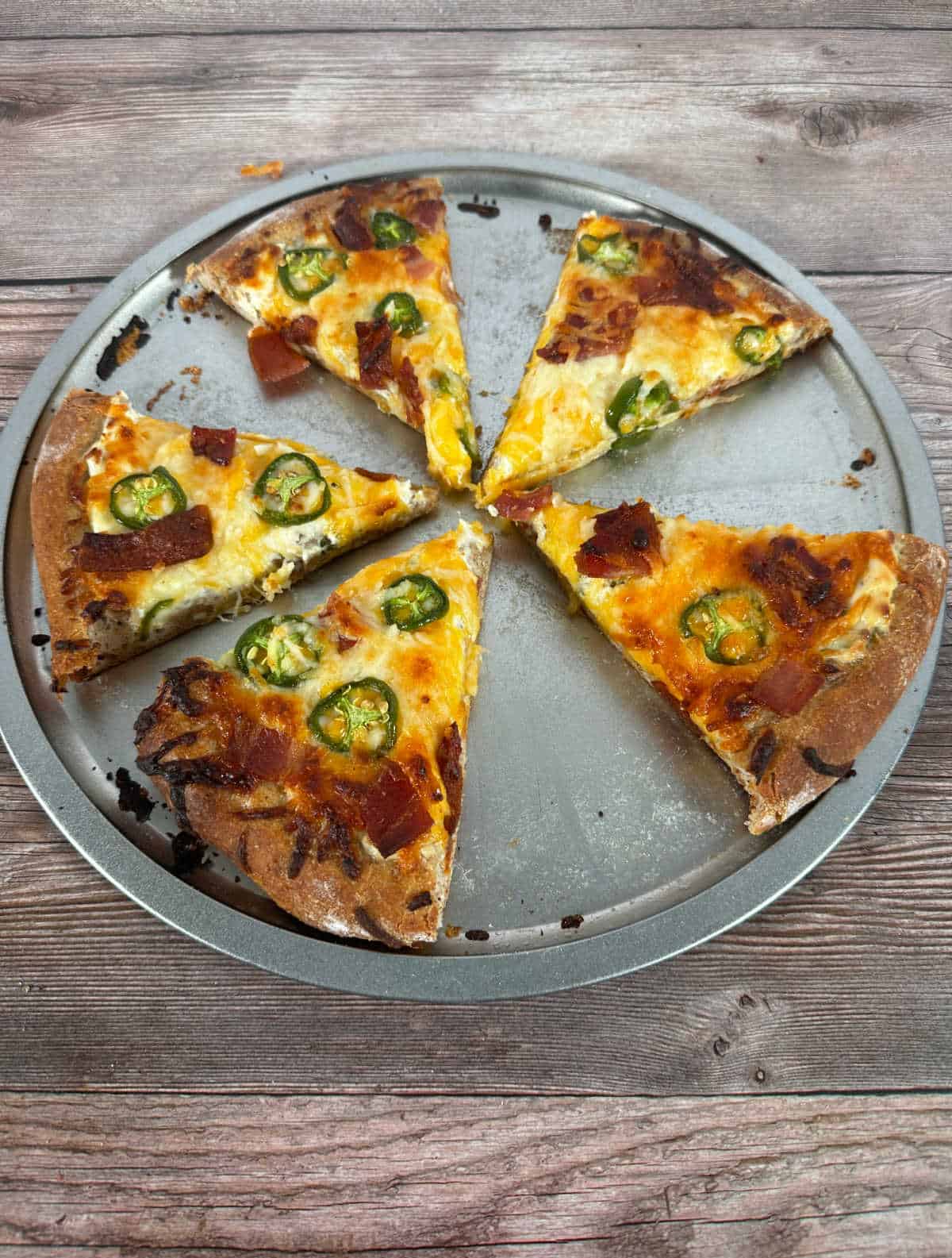 Overhead image of pizza pan with slices pulled apart - cheese is golden brown and studded with jalapeno slices and crumbled bacon.