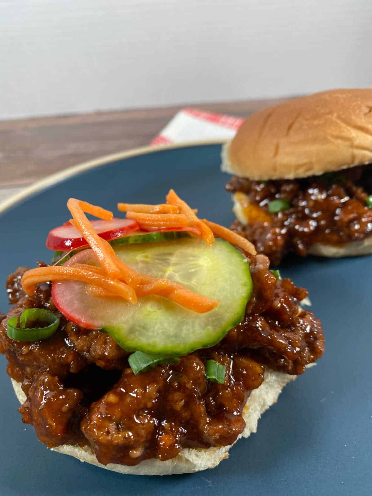 Close up of sandwich on bun, topped with pickled vegetables and green onions. 