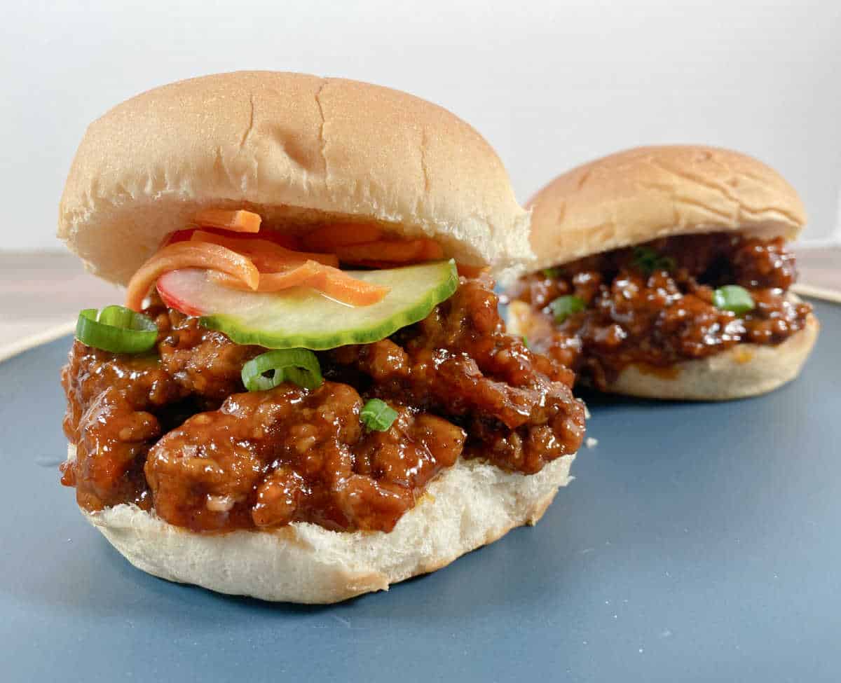 Side view of sandwiches showing the meat piled high and the pickled vegetables under the top bun. 