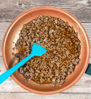 Process shot - sauce poured over cooked ground beef in a skillet. 