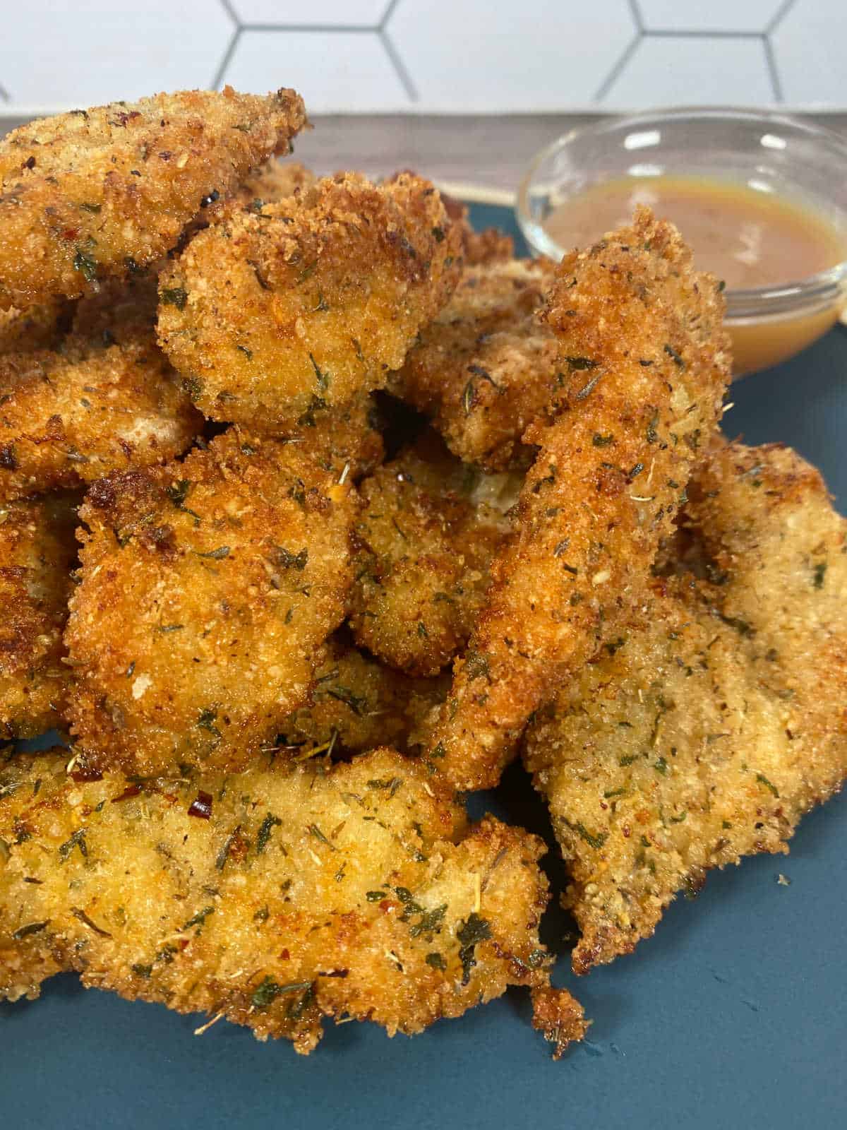 Close up of chicken tenders on a dark blue plate.