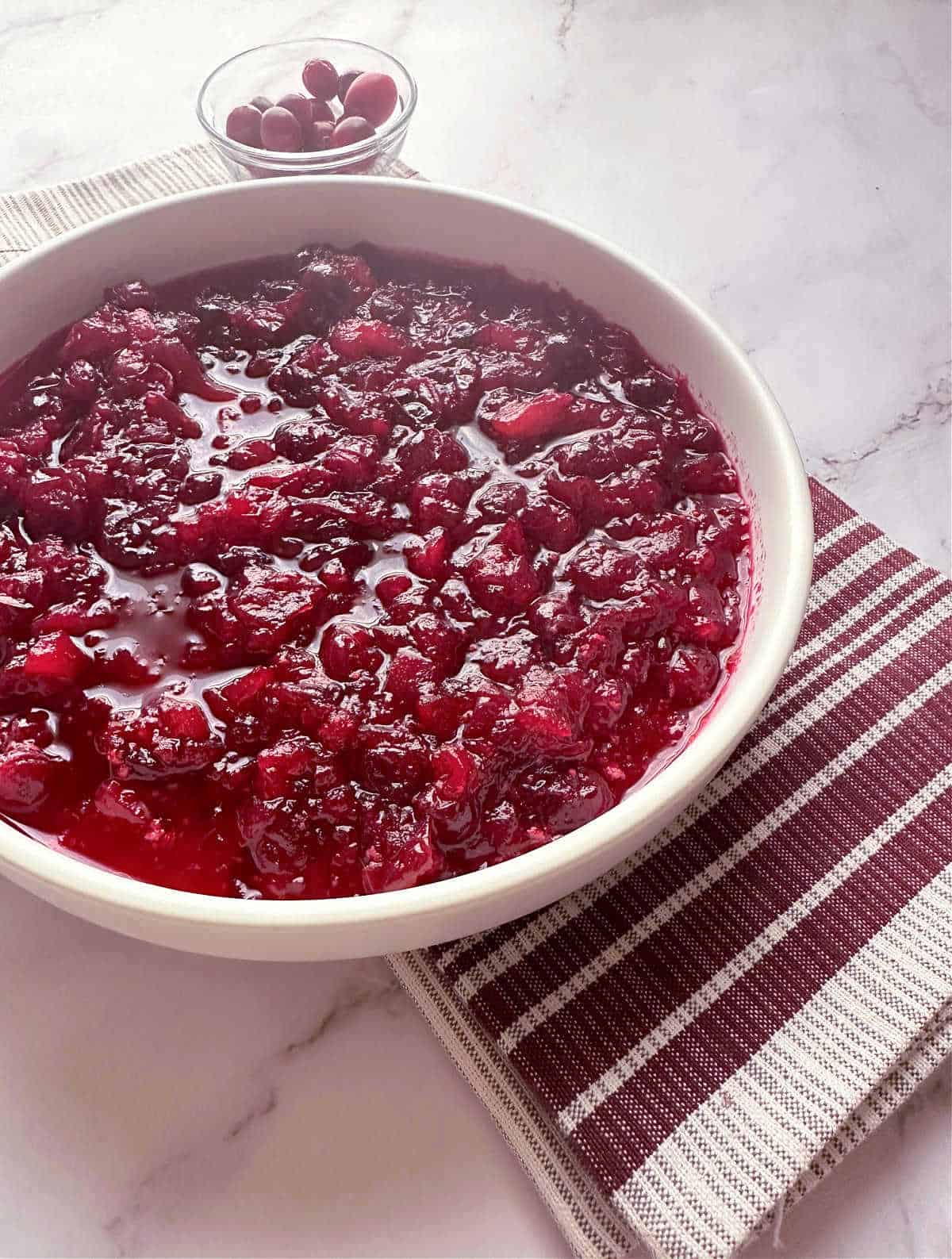 Cranberry sauce in a shallow white bowl with a burgandy and gray striped napkin underneath. 