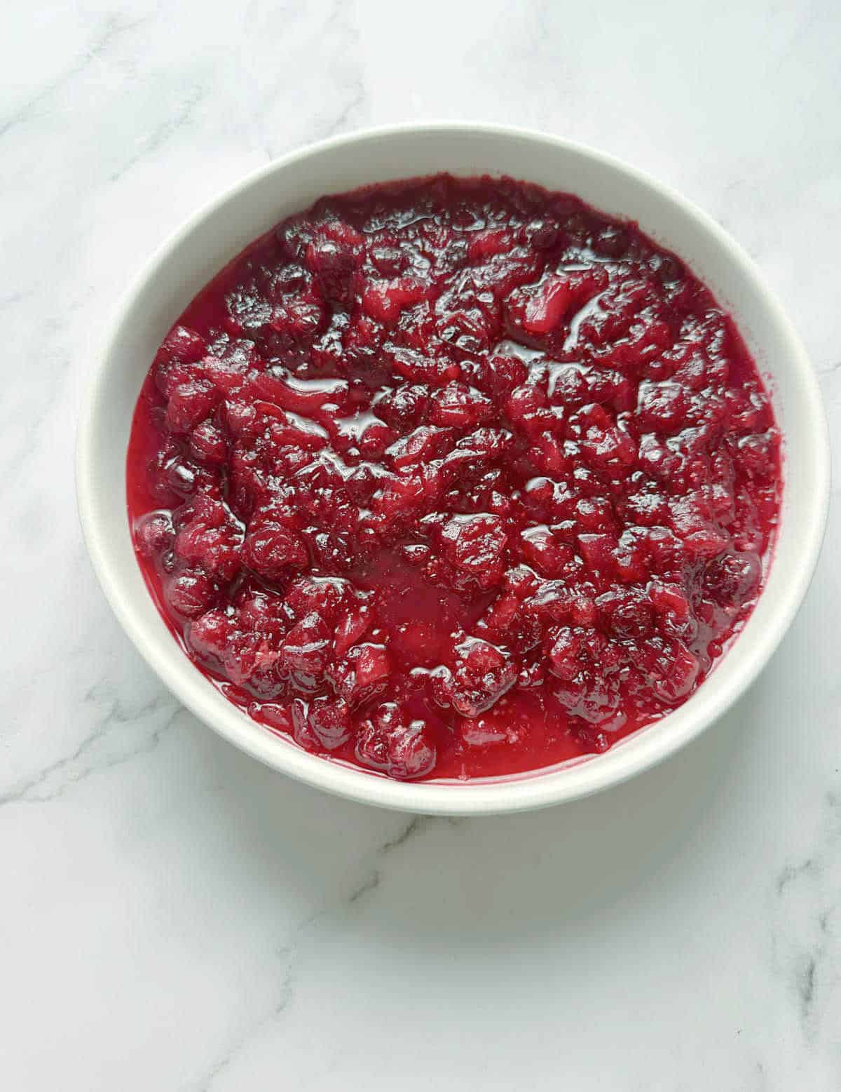 Overhead image of sauce in a shallow, white bowl on a marble background. 