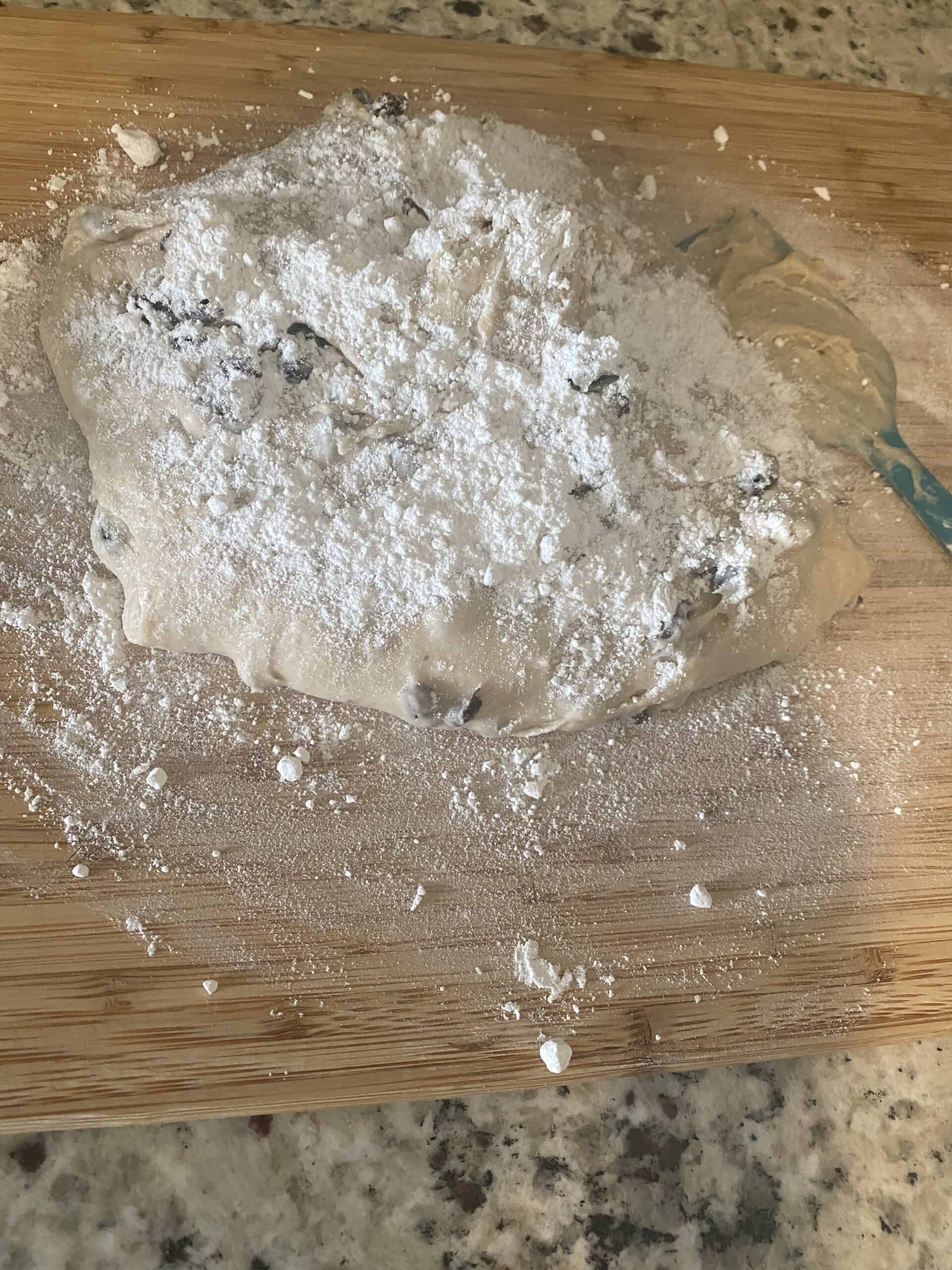 Process shot - kneaded dough, topped with flour sitting on a wooden cutting board. 