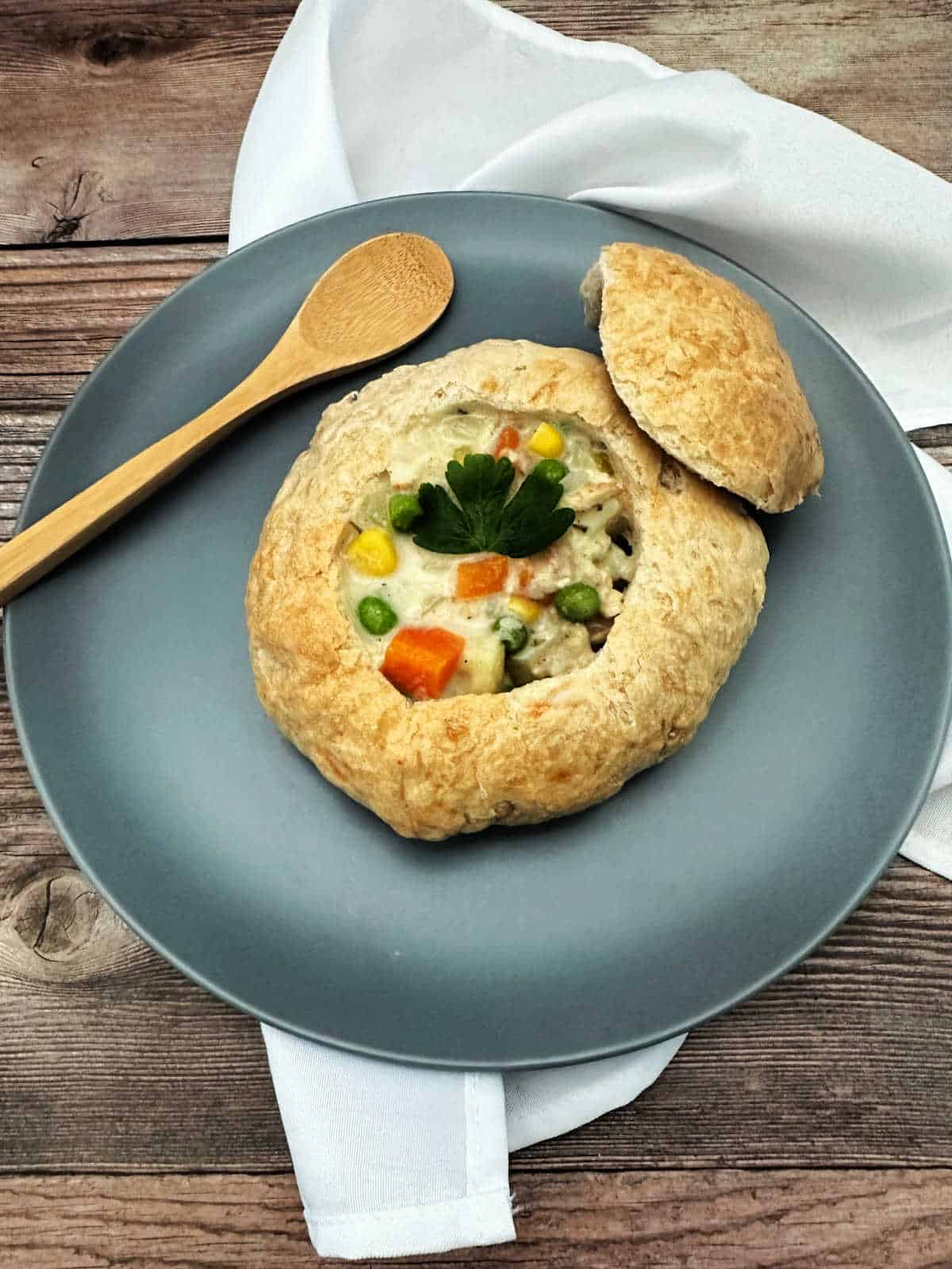 Soup sits in a bread bowl on a dusty blue plate on a wooden background.