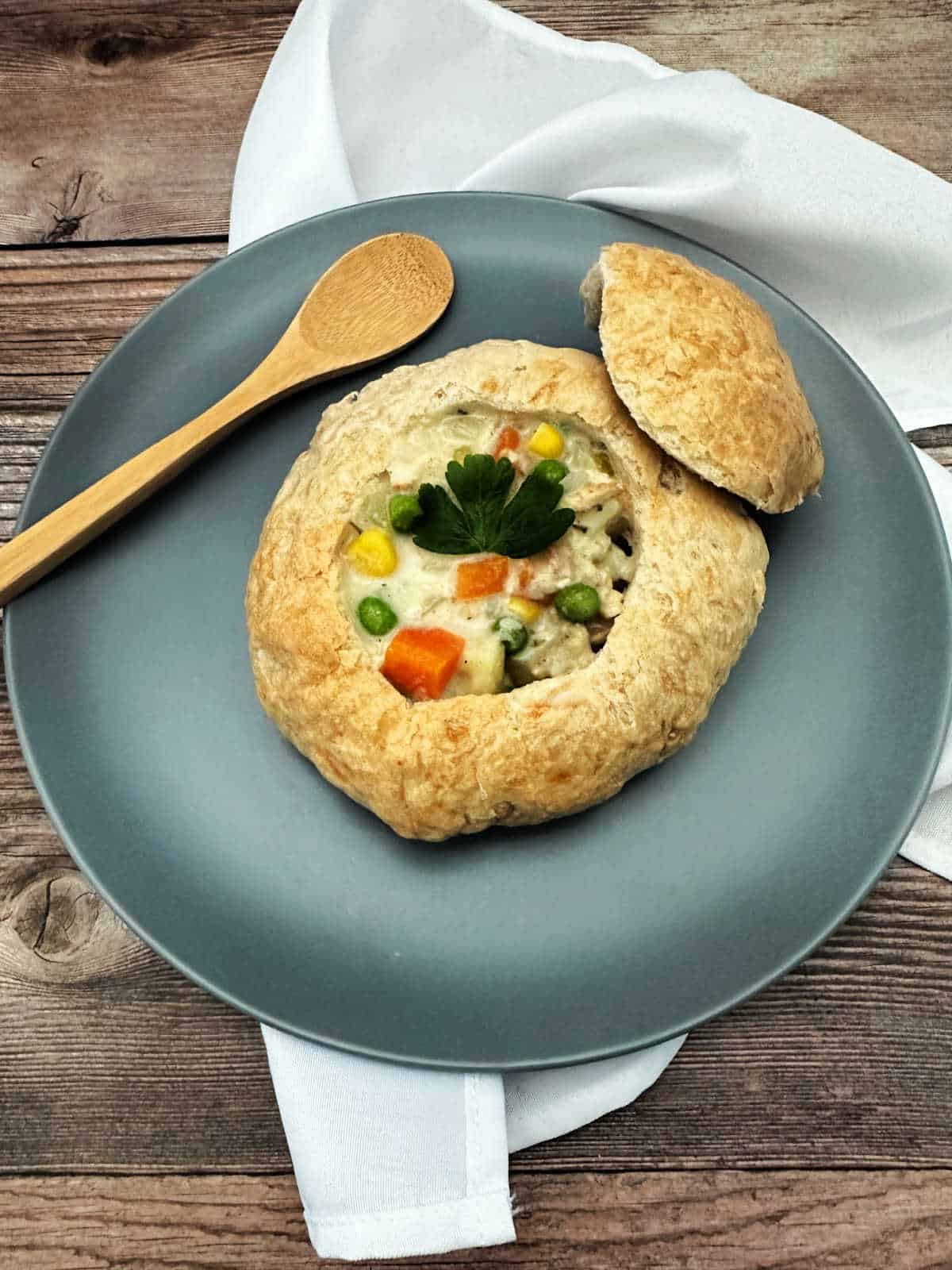 Soup sits in a bread bowl on a dusty blue plate on a wooden background. 