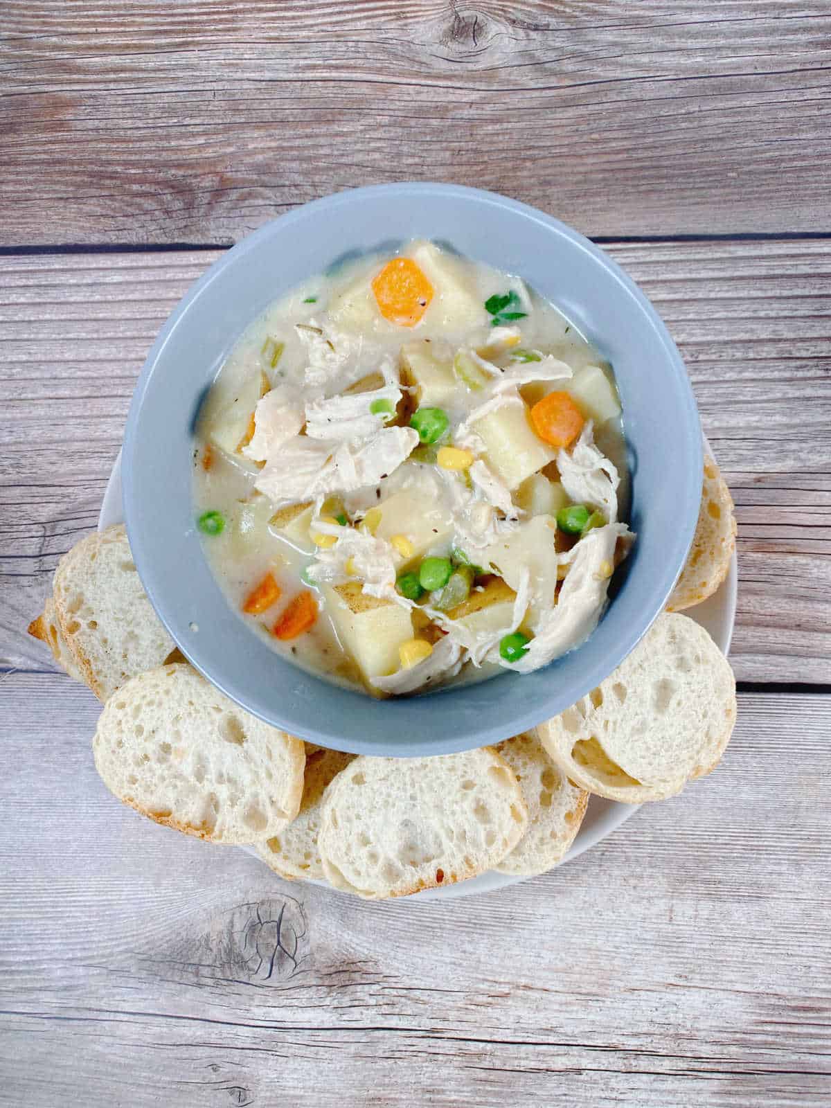 Overhead image of soup in a blue bowl, surrounded by baguette slices for alternate serving options. 